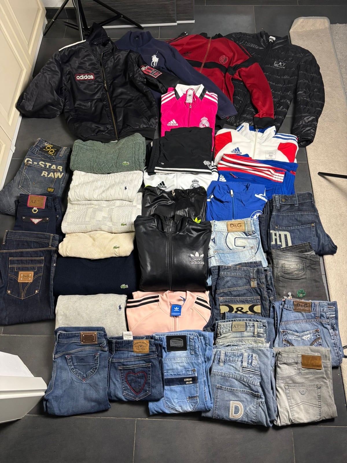 Sortierter Resell-Einkauf: Markenjacken, Strick und Designer-Jeans ausgelegt auf dem Boden